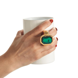 A hand holds the mug with the green gem ring.
